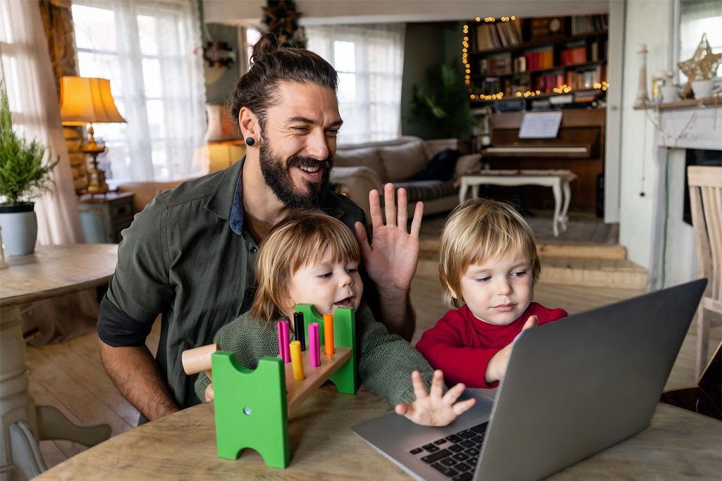 Ein Vater mit zwei Kindern winken freudig in die Laptopkamera
